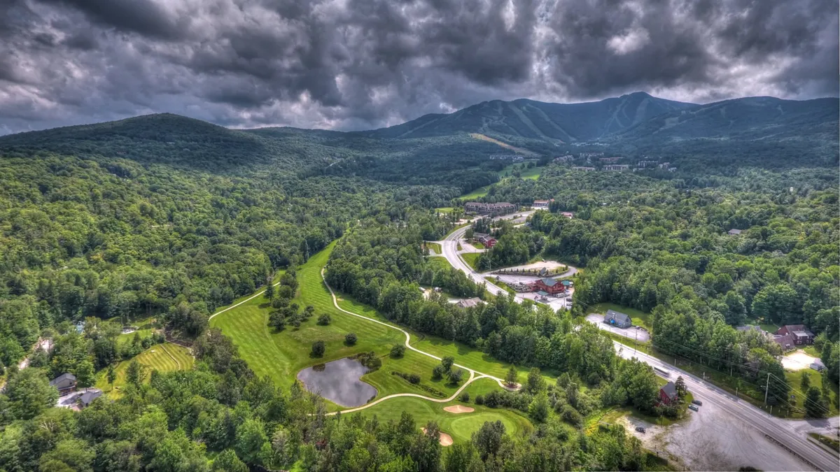 A sweeping view of mountains, a golf course, a pond, and a winding road, all bathed in tranquil light. This vista captures the expansive natural beauty surrounding the property, inviting exploration and adventure.