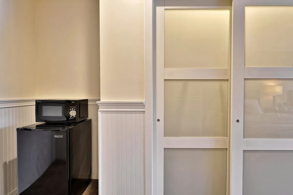 This image shows a kitchenette area with a microwave and a mini fridge beneath a countertop, set against sliding doors. The setup is tailored for preparing snacks, quick meals, or storing drinks—exactly as described in the section. The ambiance suggests comfort and ease for guests.