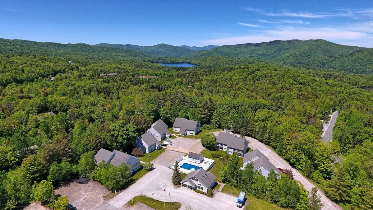 This exterior image captures a peaceful mountain landscape with a swimming pool in the foreground, scattered buildings nestled into the hillside, and a spacious outdoor area that invites exploration and relaxation. The setting sun casts a warm glow, highlighting the region's natural beauty and recreational opportunities.
