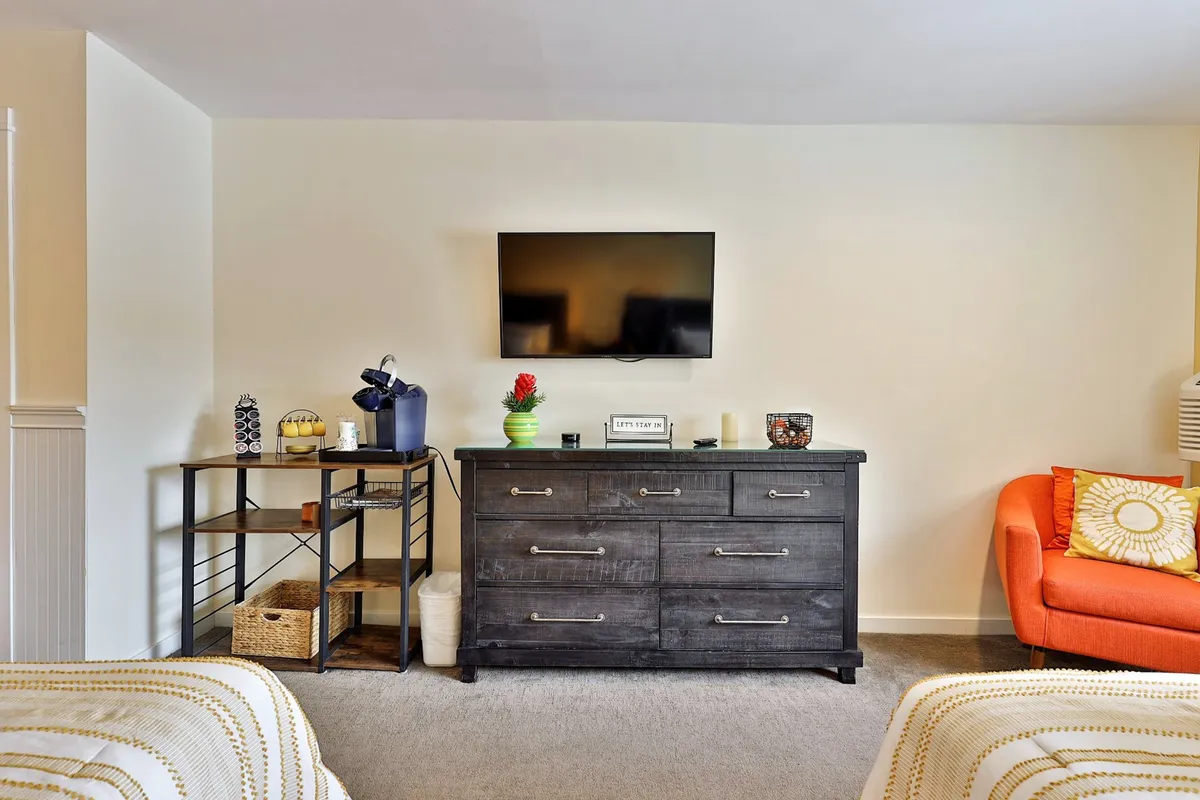 A cozy living area featuring a black dresser, an orange couch, and a wall-mounted TV. The setting is relaxed and modern, providing an inviting spot to watch TV, read, or socialize after a busy day.