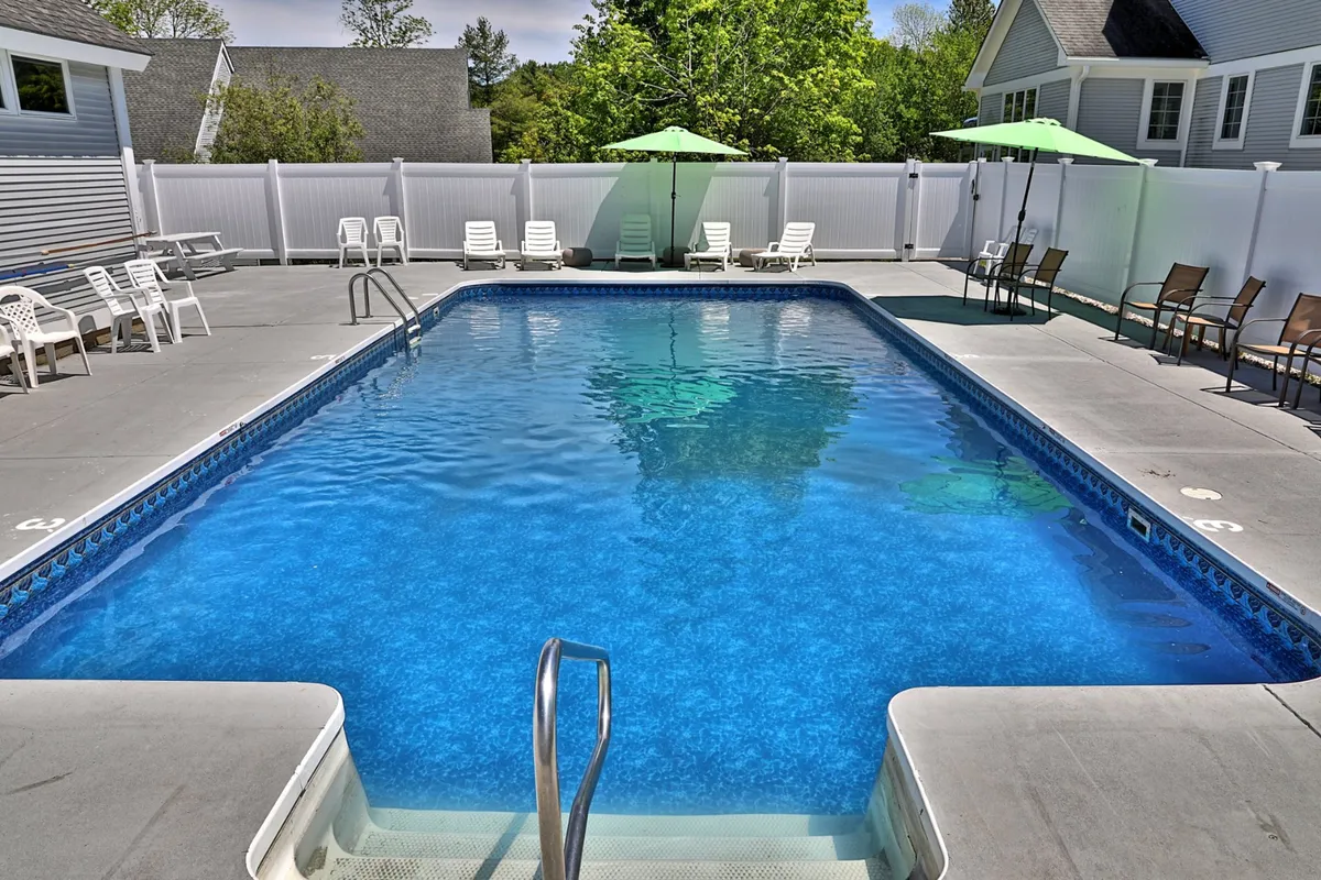 This image showcases the outdoor swimming pool surrounded by lounge chairs and green umbrellas, set against lush greenery. The pool sparkles under the summer sun, and the inviting setup suggests a perfect place for sunbathing, swimming, and poolside relaxation.