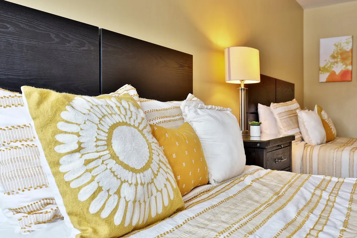 A cozy studio bedroom featuring neatly made bedding, decorative pillows, and a soft lamp glow creates an atmosphere perfect for unwinding. The space encourages relaxation—whether it's lounging with a book, enjoying a cool drink, or simply resting after a day outdoors.