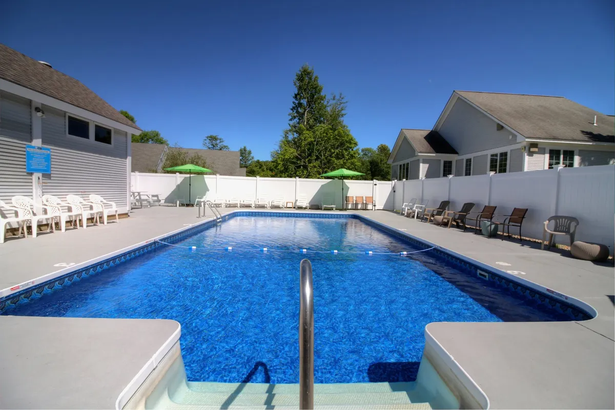 An inviting exterior shot featuring a sparkling swimming pool surrounded by lounge chairs and green umbrellas, all within a fenced area. The cheerful, sunlit atmosphere suggests a lively social setting ideal for groups and friends to unwind and socialize after a day of adventure.