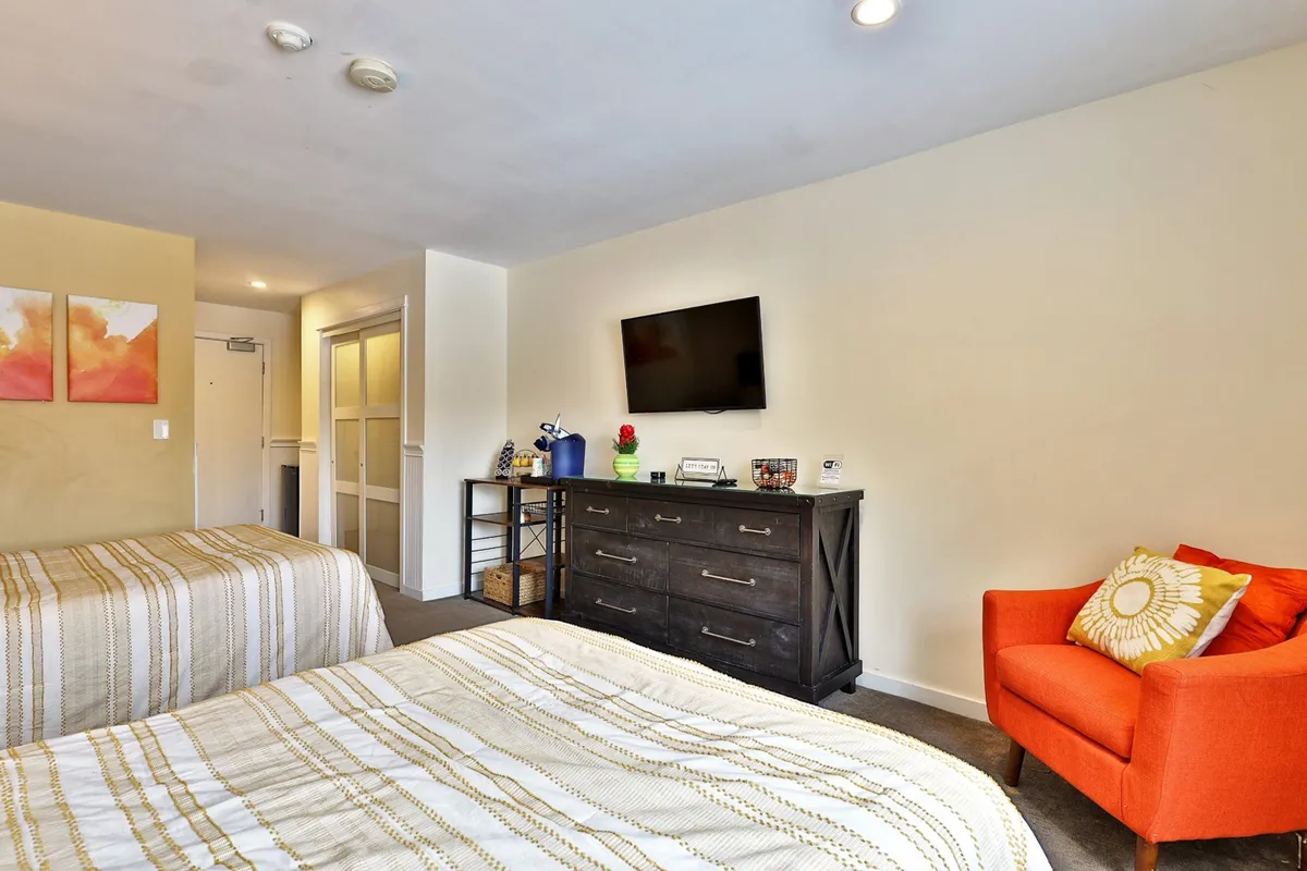 A comfortable room with two beds, an orange armchair, a dresser, and a TV. The scene suggests a perfect spot for relaxing, enjoying a movie night, or unwinding after exploring local nightlife.