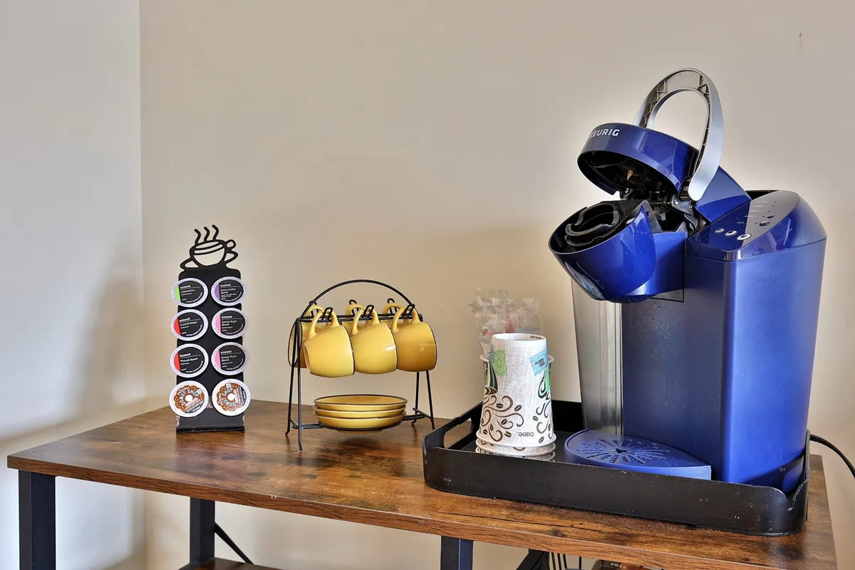 This image features an in-room coffee maker, a coffee pod holder, cheerful yellow mugs, and paper towels arranged on a compact counter. The setting is cozy and inviting, capturing the essence of morning routines or a quick coffee break during the day.