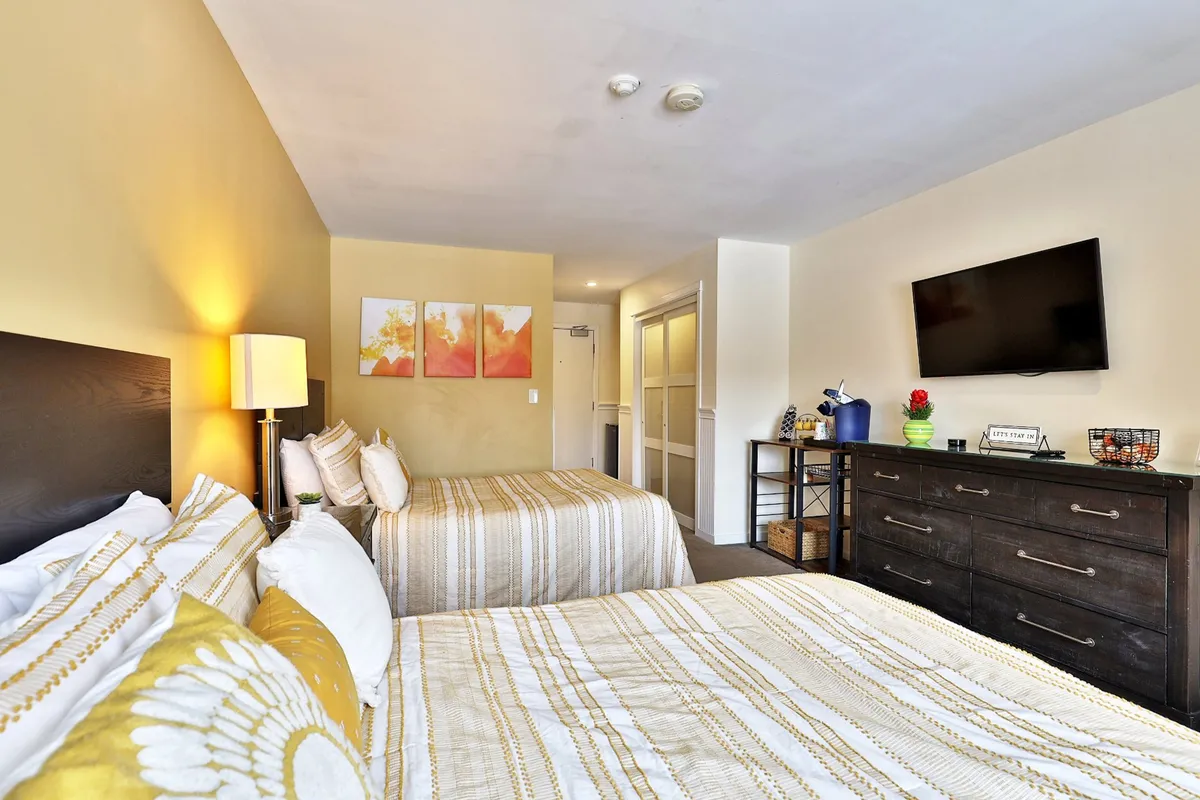 This image features two beds with striped bedding, framed artwork on the wall, a flat-screen TV, and a nightstand with a lamp. The room feels bright and inviting, showcasing both the sleeping and entertainment amenities. The arrangement suggests comfort and social connection, ideal for relaxing after a day outdoors.